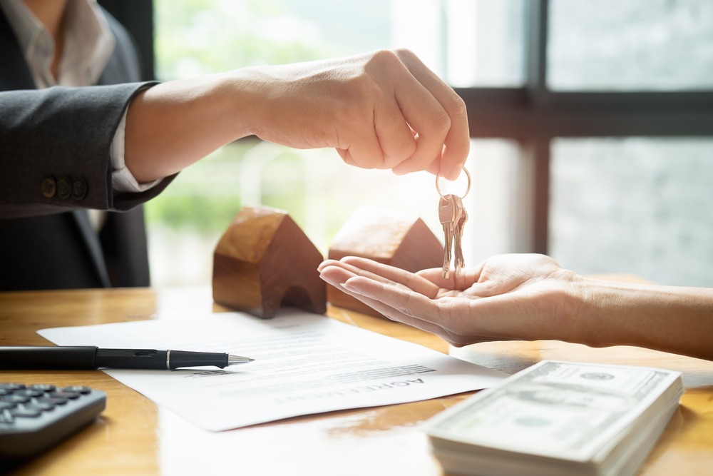 image of a man's hand handing over keys to a woman's hand, as part of a real estate transaction with a real estate brokerage.