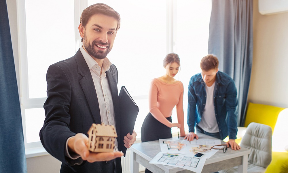 a real estate agent standing in front of clients holding a miniature house.