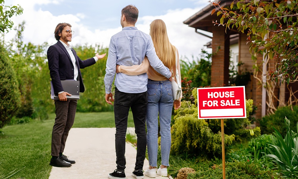 Real estate broker showing house for sale to young couple, outside