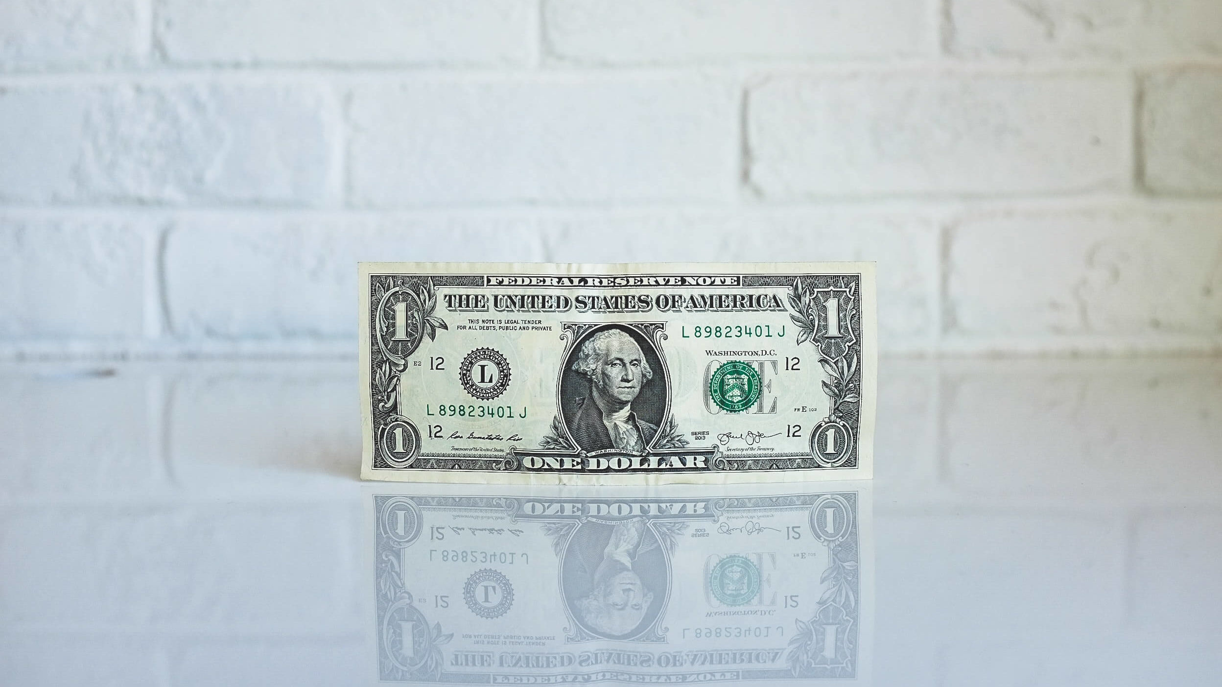 dollar bill in front of a white brick wall, representing marketing budget for your geo farm in real estate